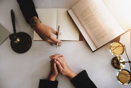 bird's eye view of a legal desk with scale of justice, a gavel, people's hands, and various paperwork